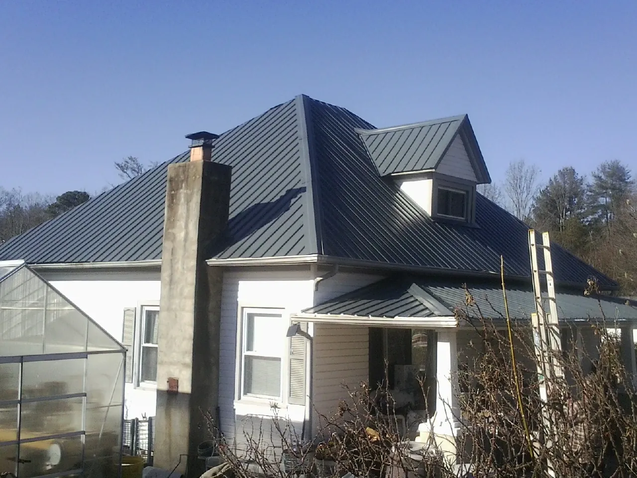 Dark blue standing seam metal roof on a white farmhouse with dormer — Slate & Tile Roof Repair by Roofing Brothers in Eight Mile