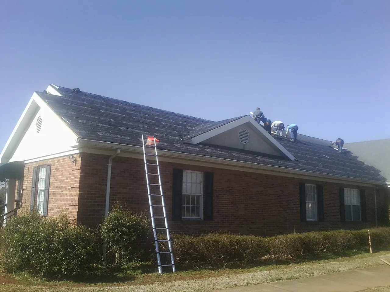 Crew tearing shingles off a brick ranch roof with a ladder set — Metal Roof Repair work by our crew in Eight Mile