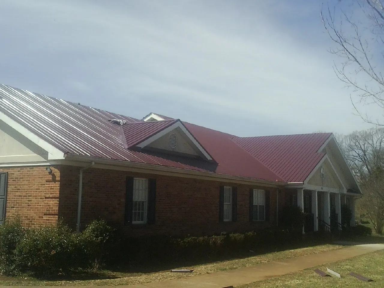 Red metal roof with gabled entries on a long brick building, from a Hail Damage Roof Repair job in Eight Mile