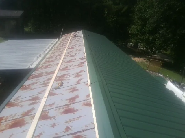 Old rusted panels beside newly installed green metal roofing — Wind Damage Roof Repair by Roofing Brothers in Eight Mile