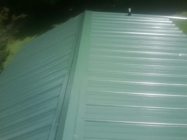 New green metal panels meeting at the ridge of a roof — Flat Roof Repair work by our crew in Eight Mile