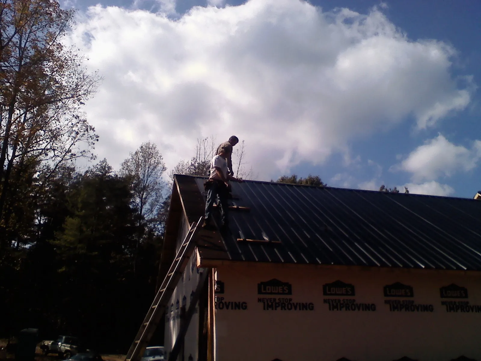 Roofer fastening dark metal panels high against a cloudy sky, from a Roof Inspection job in Eight Mile