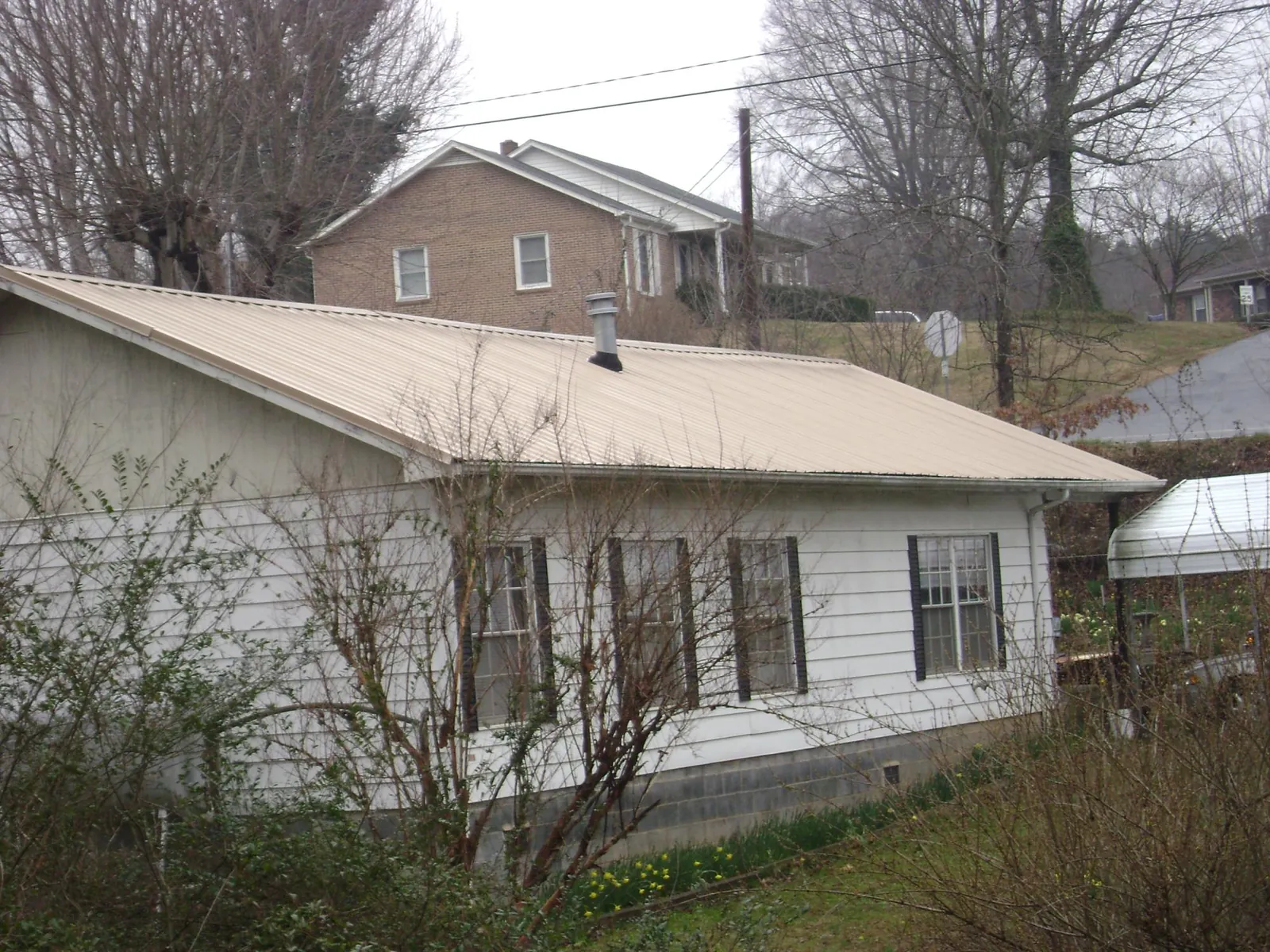Tan metal roof on a white sided house set into a hillside — Commercial Roofing by Roofing Brothers in Eight Mile