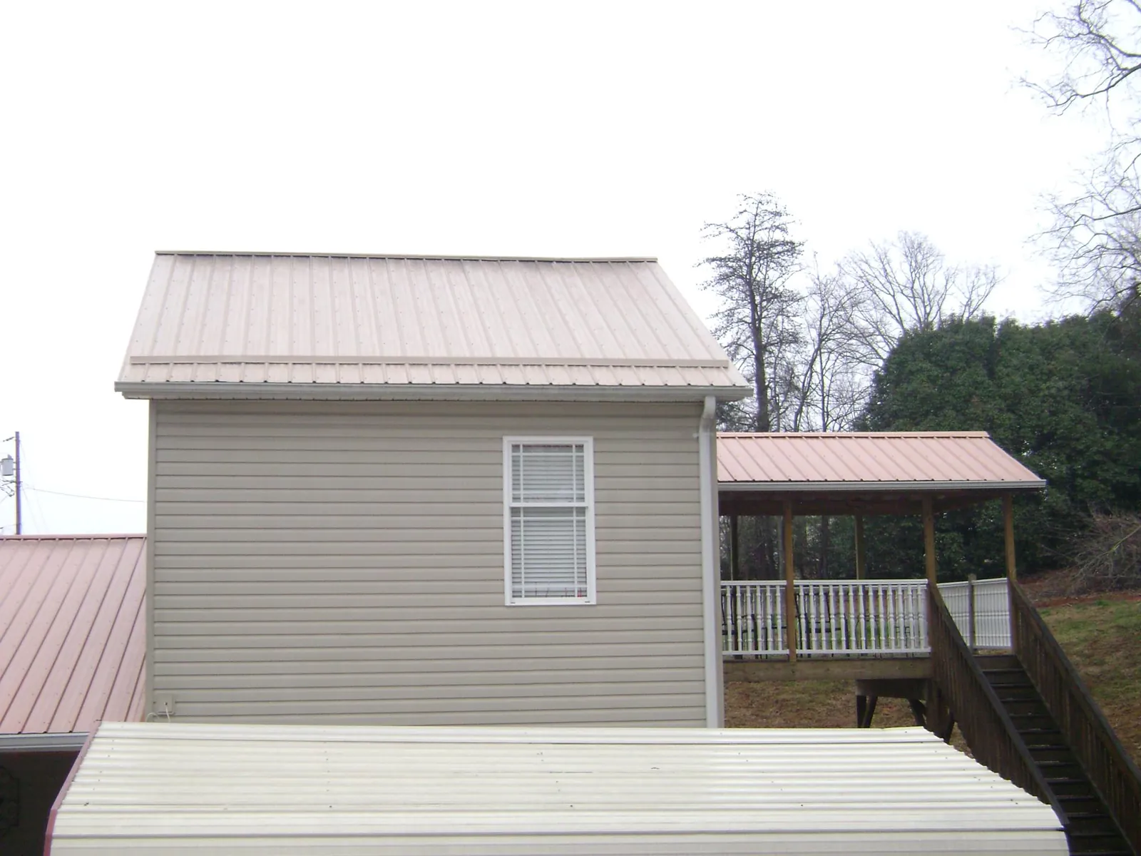 Tan metal roofs on a two story addition and attached porch, from a Roof Replacement job in Eight Mile